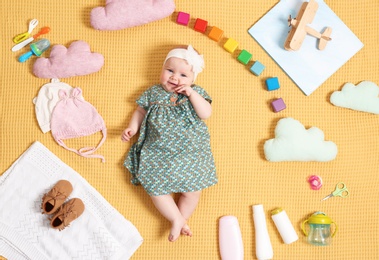 Cute little baby with clothing and accessories on color blanket, top view