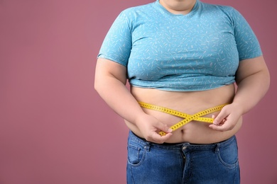 Overweight woman with measuring tape on color background