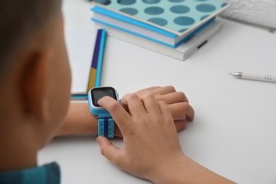 Boy with stylish smart watch at white table, closeup