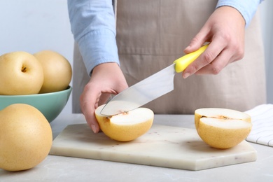 Photo of Woman cutting ripe apple pear at table, closeup