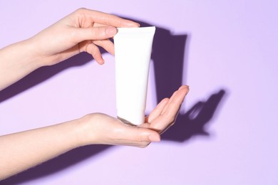 Woman holding tube of cream on violet background, closeup