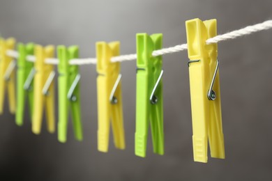 Photo of Colorful plastic clothespins on rope against grey background, closeup