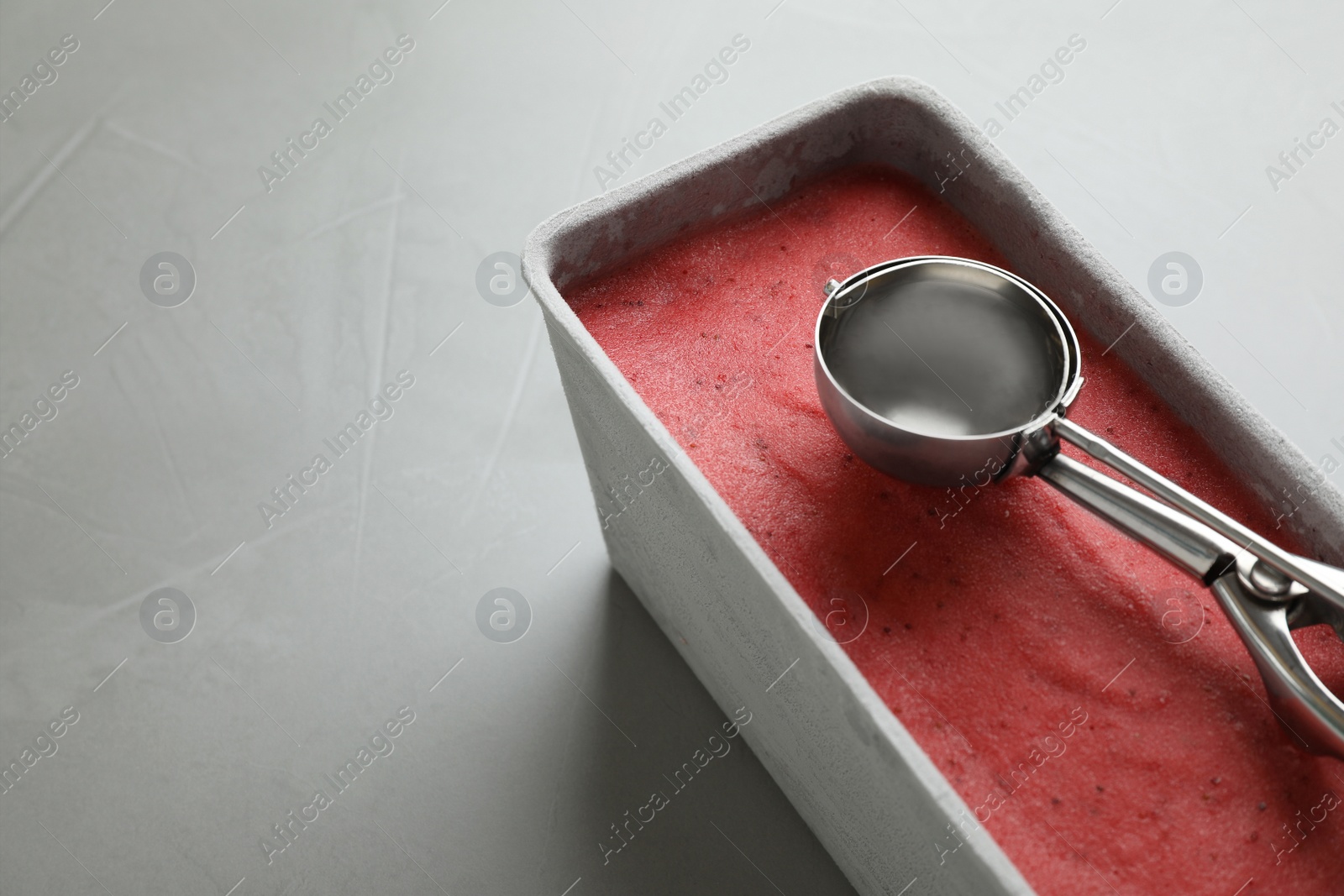 Photo of Container with delicious pink ice cream and scoop on grey table