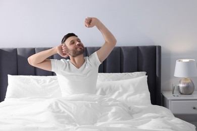 Photo of Handsome man stretching in soft bed at home in morning