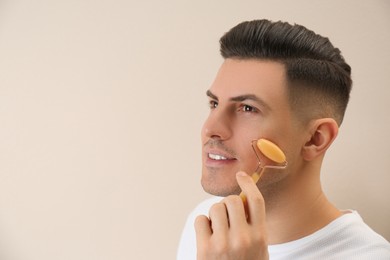 Photo of Man using mineral facial roller on beige background. Space for text