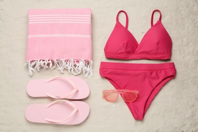 Stylish bikini and beach accessories on sand, flat lay