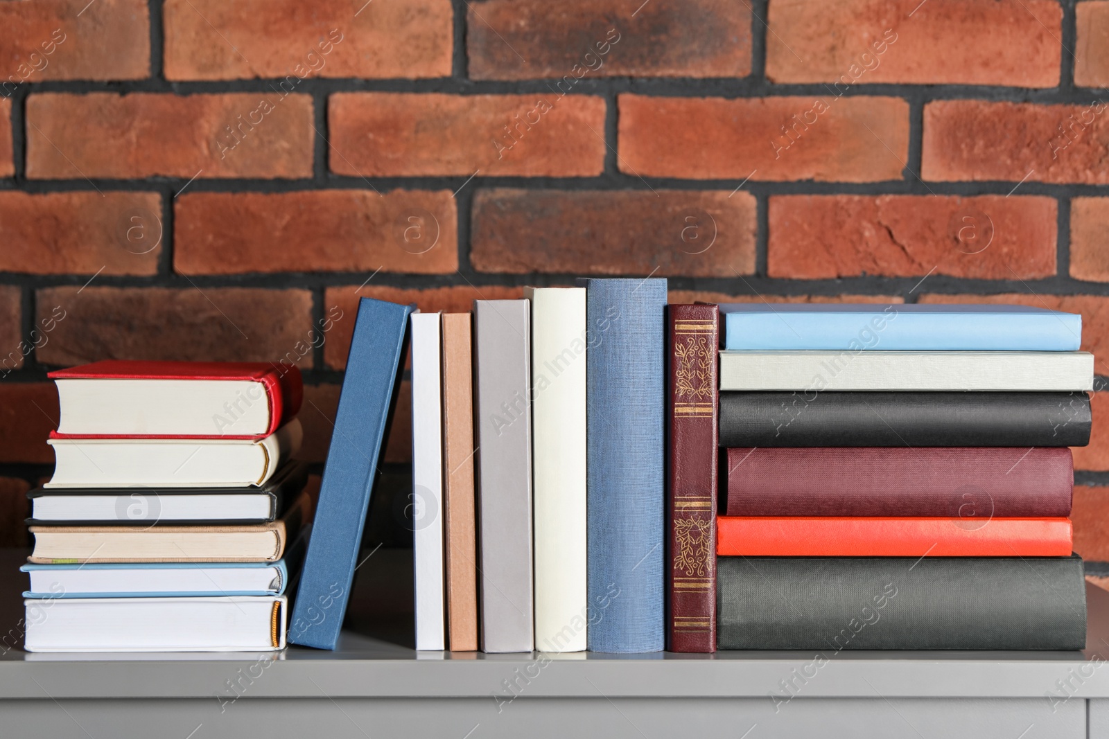 Photo of Many hardcover books on table near brick wall