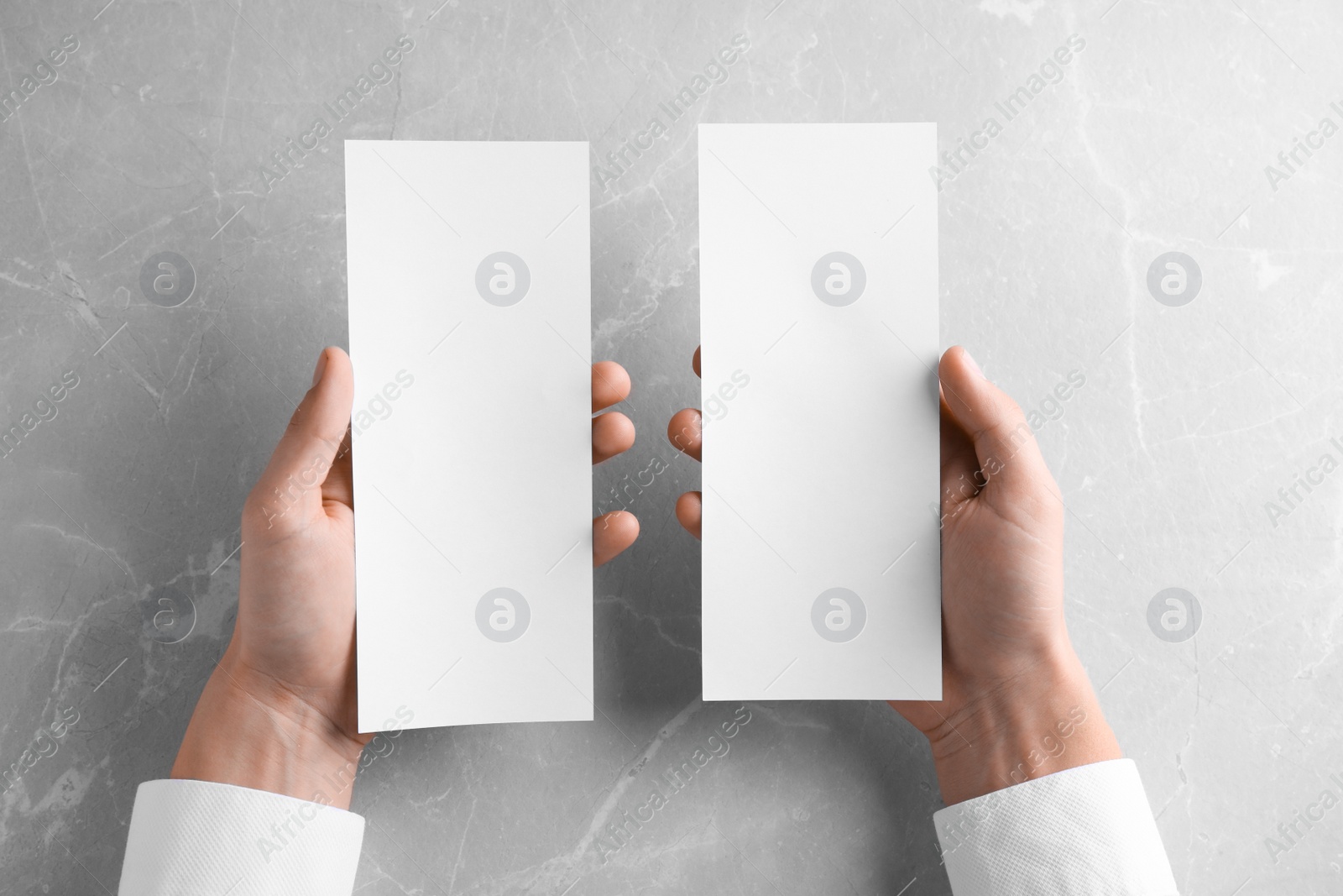 Photo of Man holding blank palm cards at light grey marble table, top view. Mock up for design