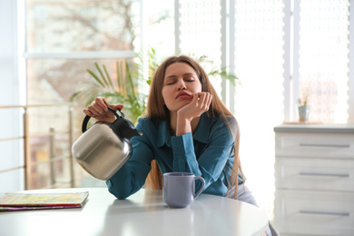 Photo of Sleepy young woman pouring coffee into cup at home in morning