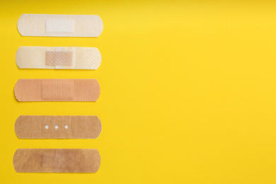 Photo of Different types of sticking plasters on yellow background, flat lay. Space for text