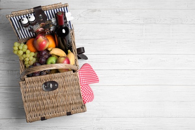 Wicker picnic basket with wine and different products on wooden table, top view. Space for text