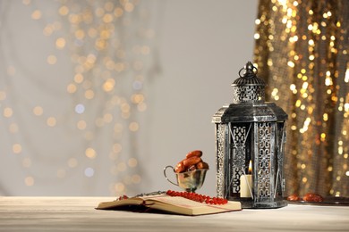 Photo of Arabic lantern, Quran, misbaha and dates on table against blurred lights, space for text