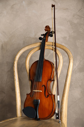 Photo of Classic violin and bow on chair against beige background