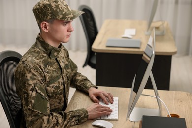 Military service. Young soldier working with computer at wooden table in office