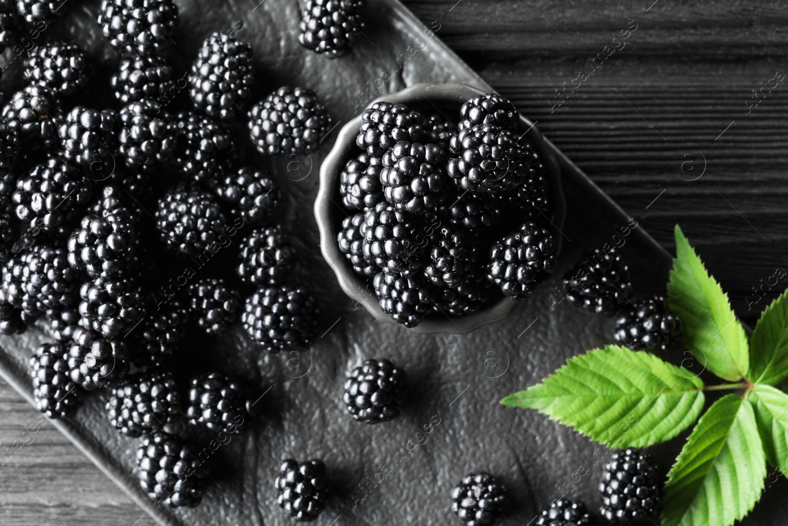 Photo of Fresh ripe blackberries and leaves on black wooden table, flat lay