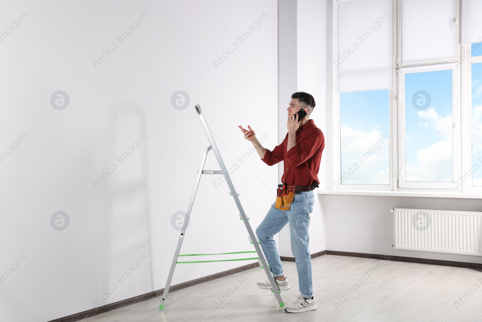 Photo of Handyman talking on phone while climbing up stepladder in room