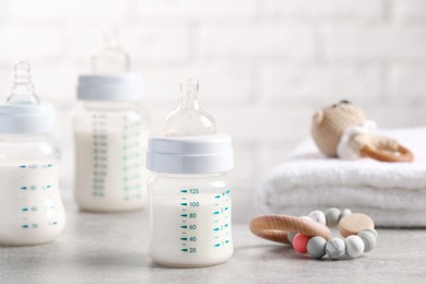 Photo of Feeding bottle with milk, baby toys and towel on light grey table