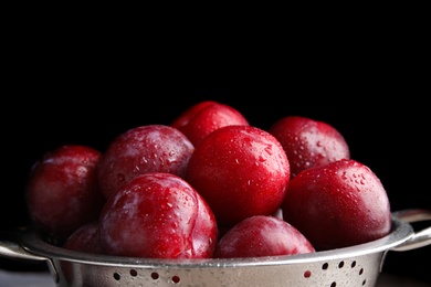 Photo of Delicious ripe plums in colander on black background, closeup