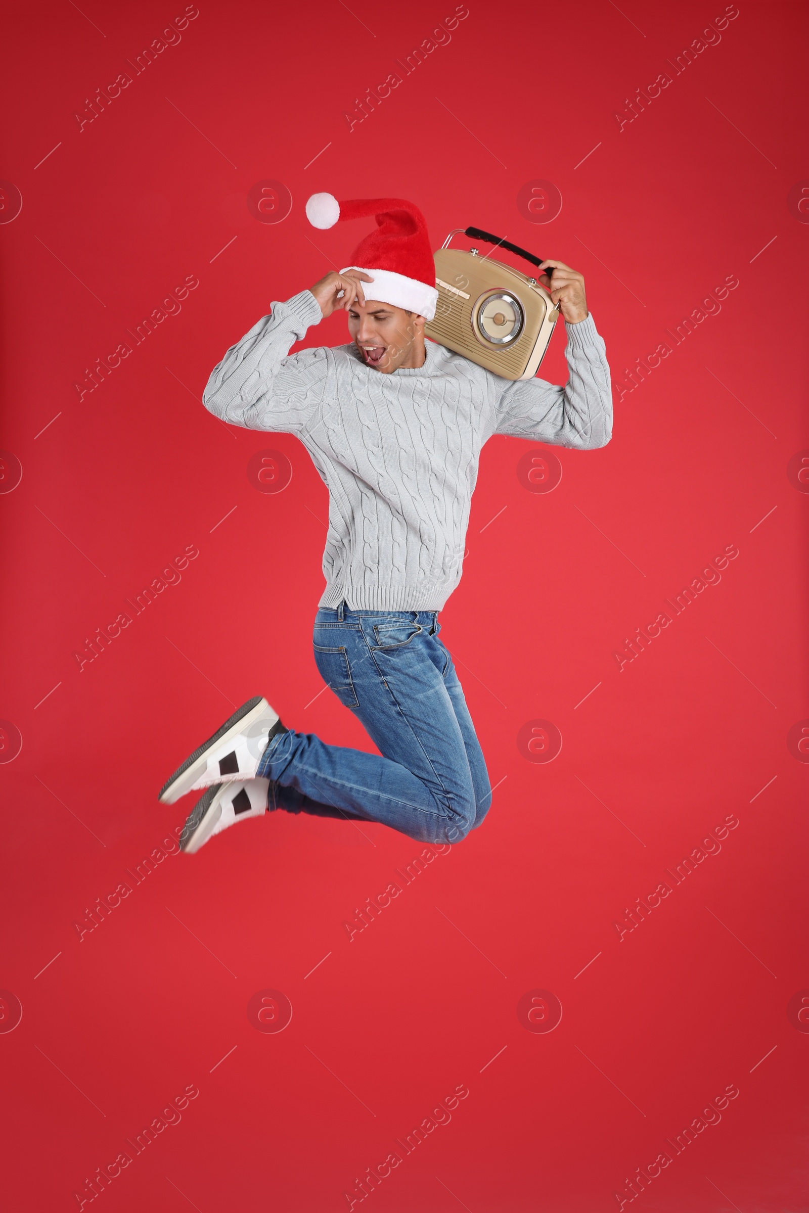 Photo of Emotional man with vintage radio jumping on red background. Christmas music