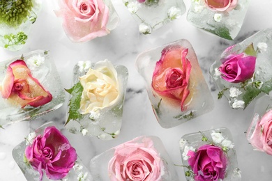 Photo of Ice cubes with flowers on marble background, flat lay