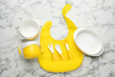 Flat lay composition with silicone baby bib and plastic dishware on white marble background