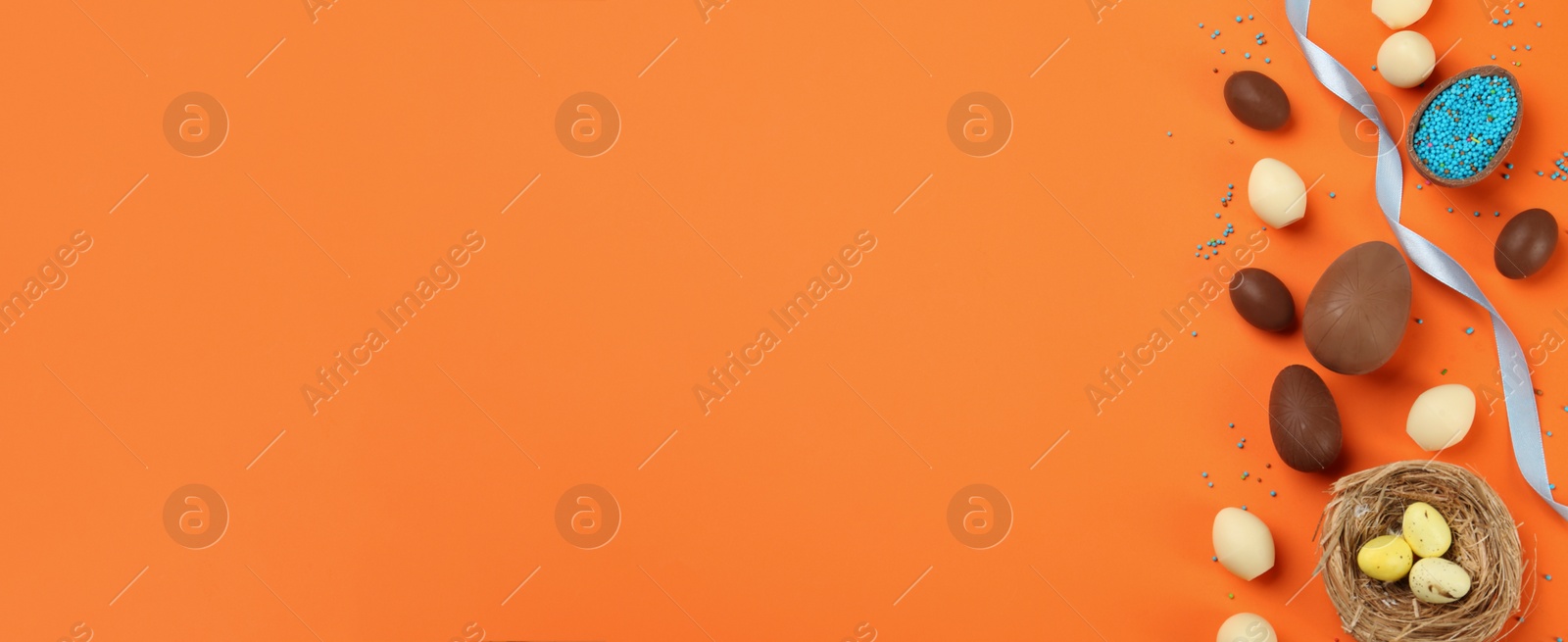 Image of Sweet chocolate eggs on orange background, flat lay with space for text. Banner design