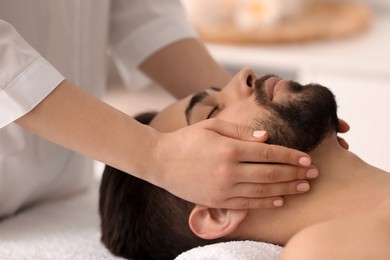 Young man receiving facial massage in beauty salon, closeup