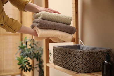 Photo of Woman putting towels into storage basket indoors, closeup