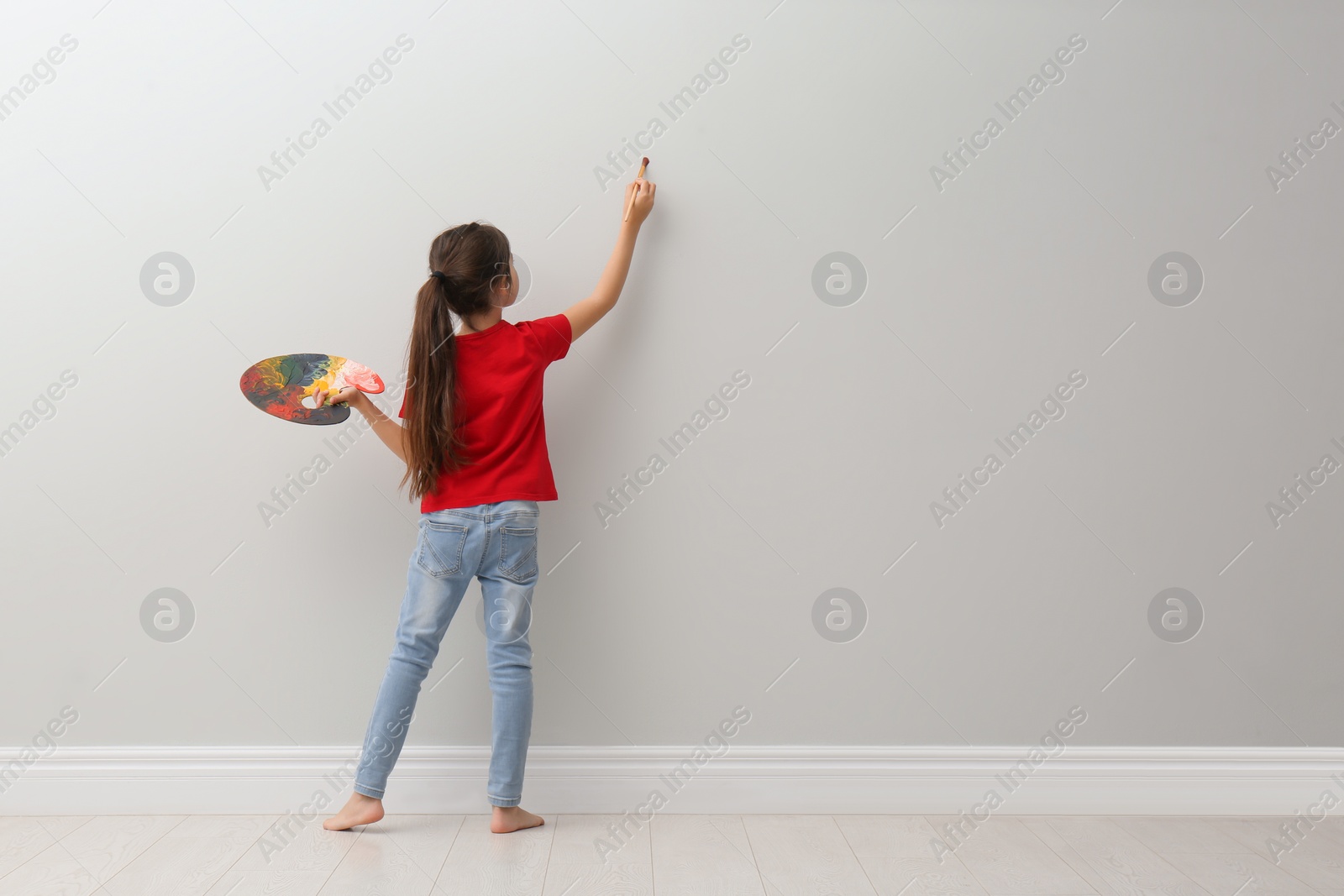 Photo of Little girl painting on light grey wall indoors, back view. Space for text