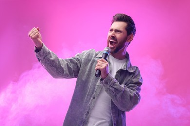 Handsome man with microphone singing on pink background