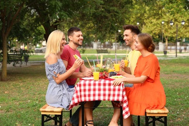 Photo of Group of people having picnic at table in park on summer day
