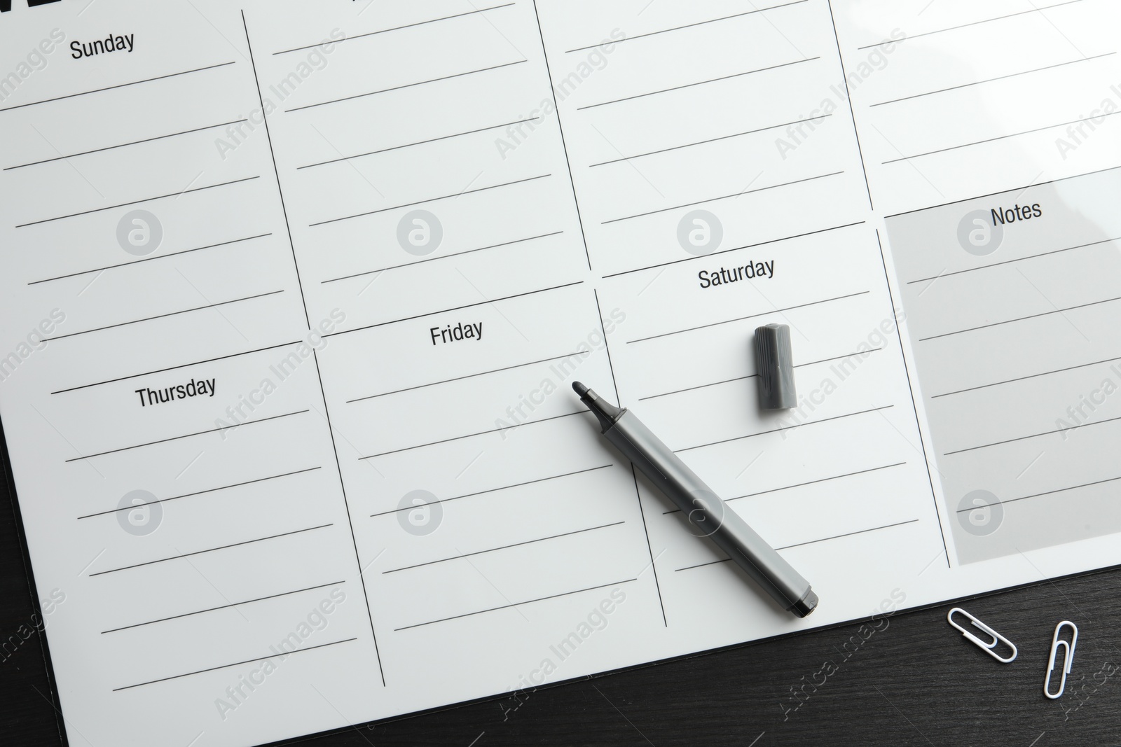 Photo of Timetable. Weekly planner, felt pen and paper clips on black wooden table, top view