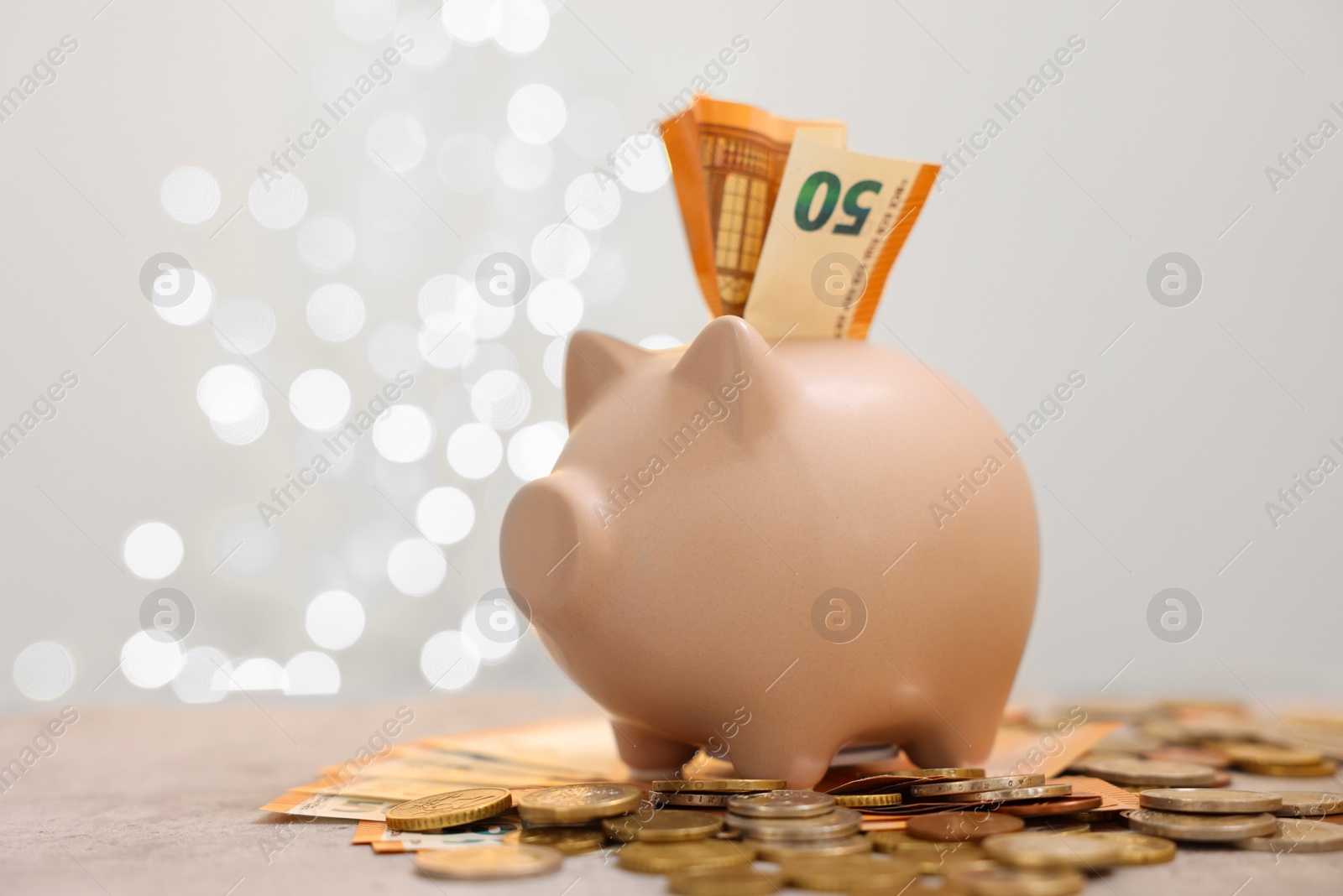 Photo of Piggy bank with euro banknote and coins on grey table against blurred lights