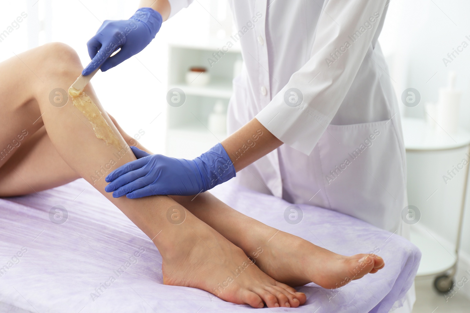 Photo of Woman getting wax epilation of legs in salon, closeup