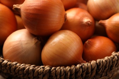 Photo of Wicker basket with many ripe onions on table, closeup