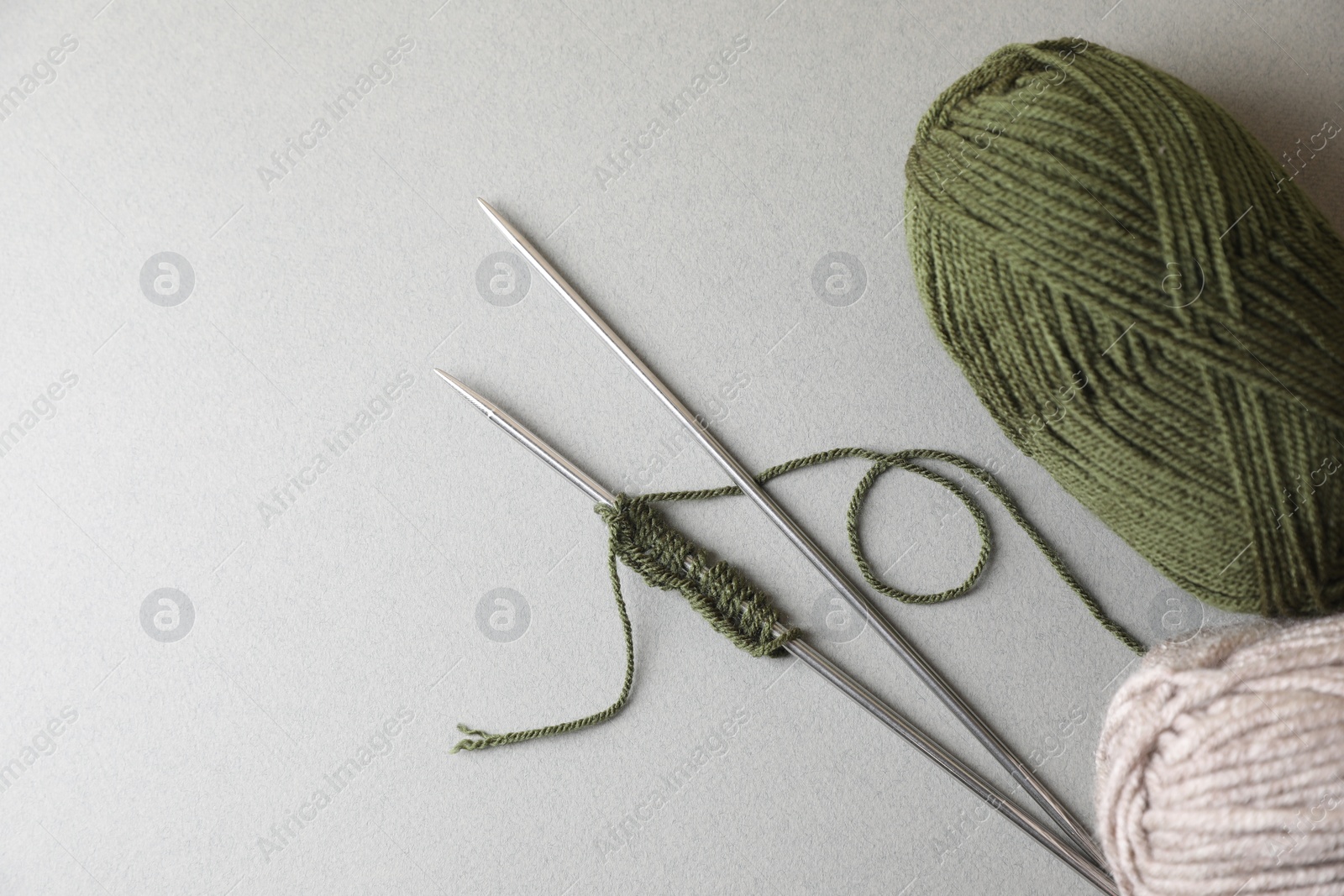 Photo of Soft green yarns, knitting and metal needles on light background, flat lay. Space for text