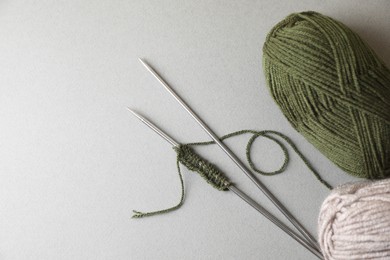 Soft green yarns, knitting and metal needles on light background, flat lay. Space for text