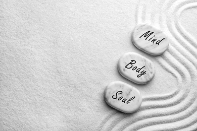 Image of Stones with words Mind, Body, Soul on sand, flat lay. Zen and harmony 