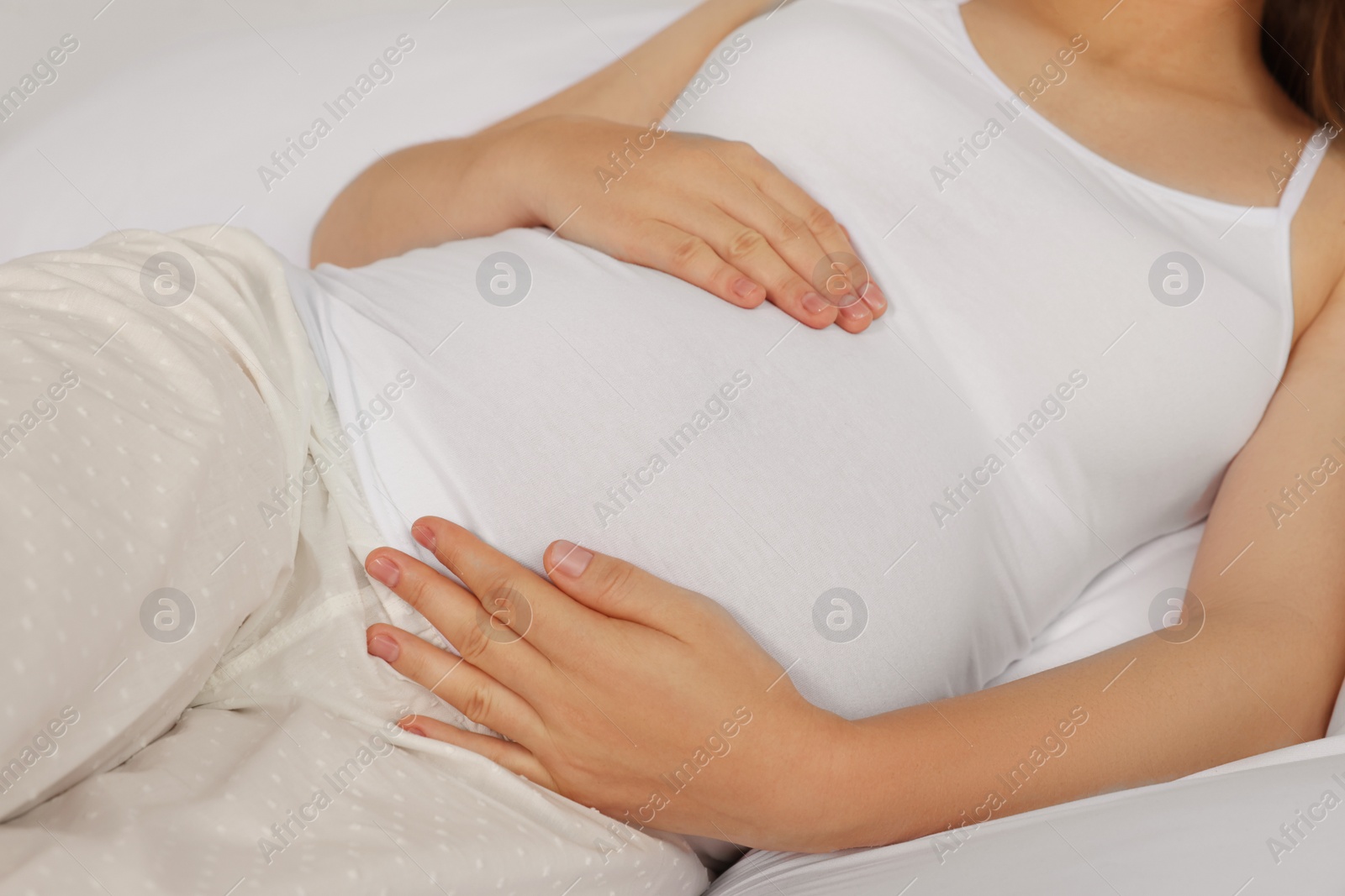 Photo of Pregnant woman in pajamas lying on bed, closeup