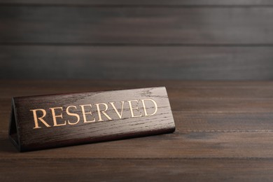 Photo of Elegant sign RESERVED on wooden surface, space for text. Table setting element