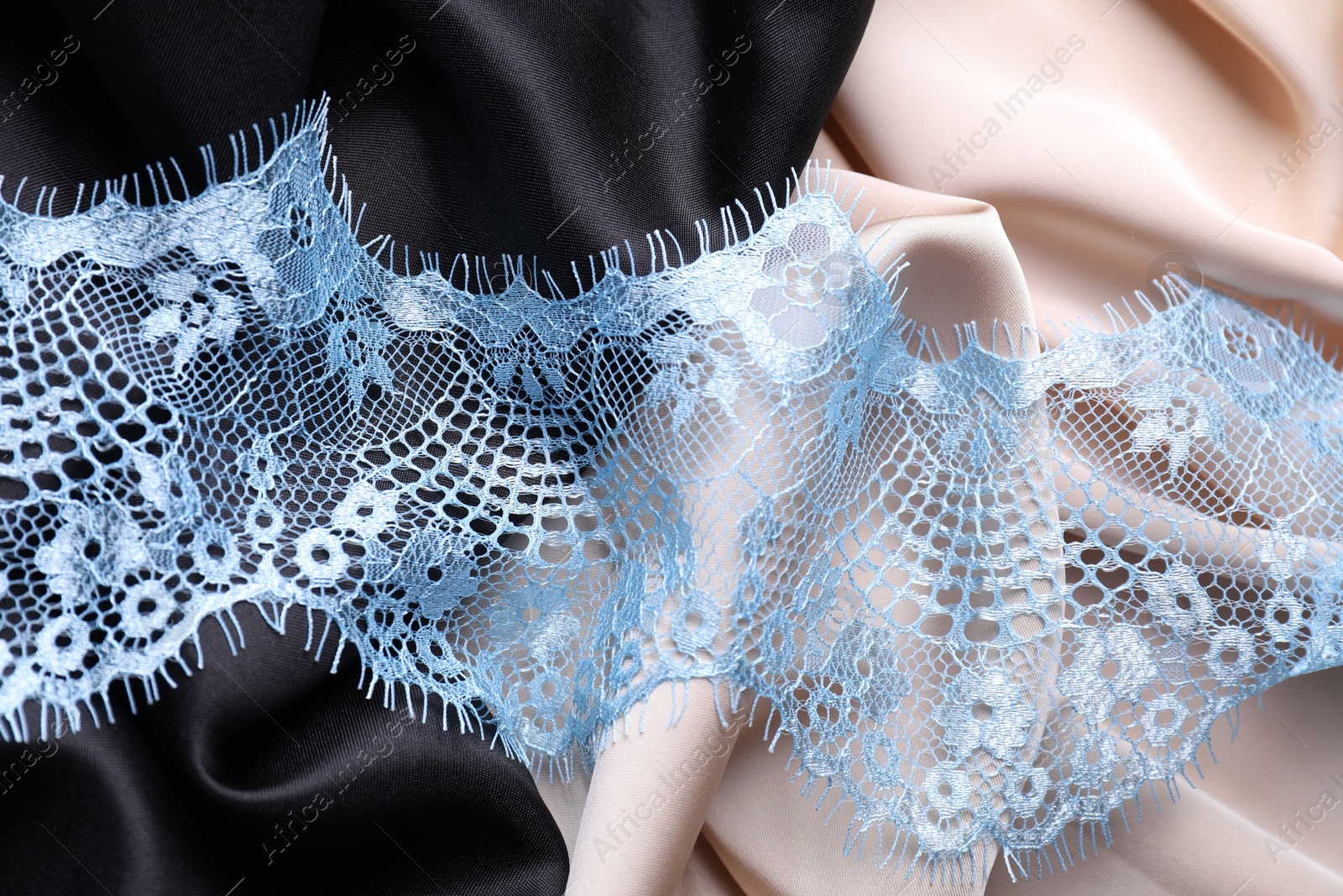 Photo of Beautiful light blue lace on color fabrics, top view