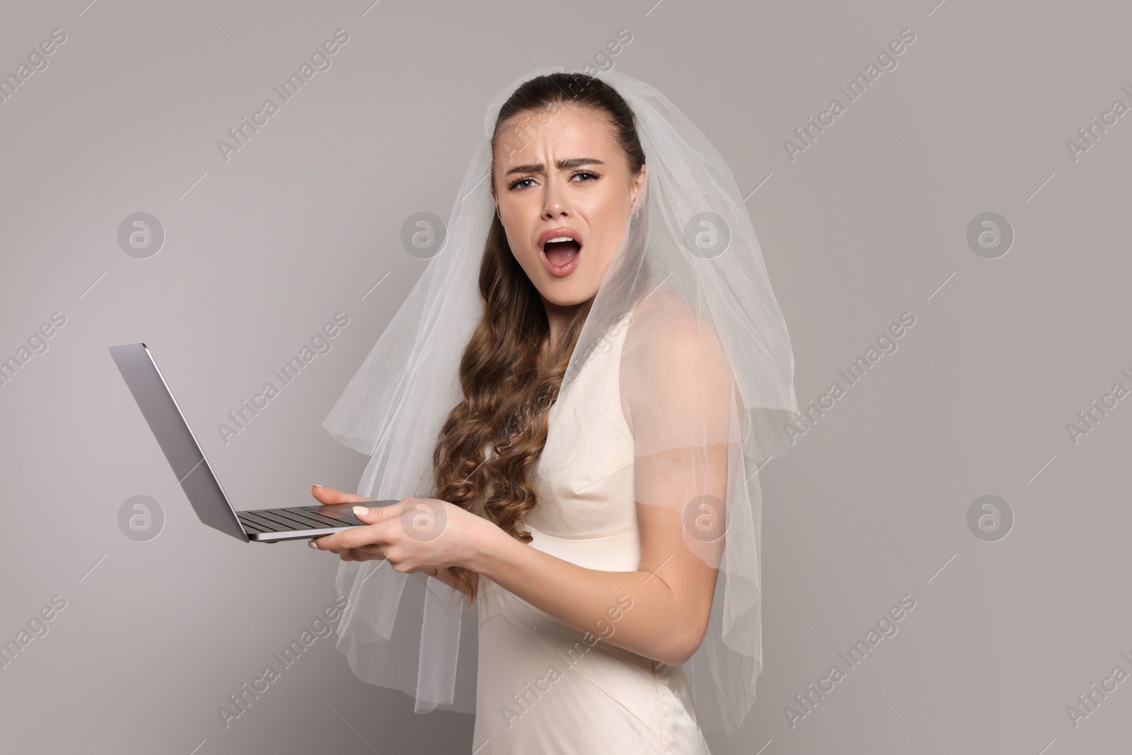 Photo of Shocked bride with laptop on gray background