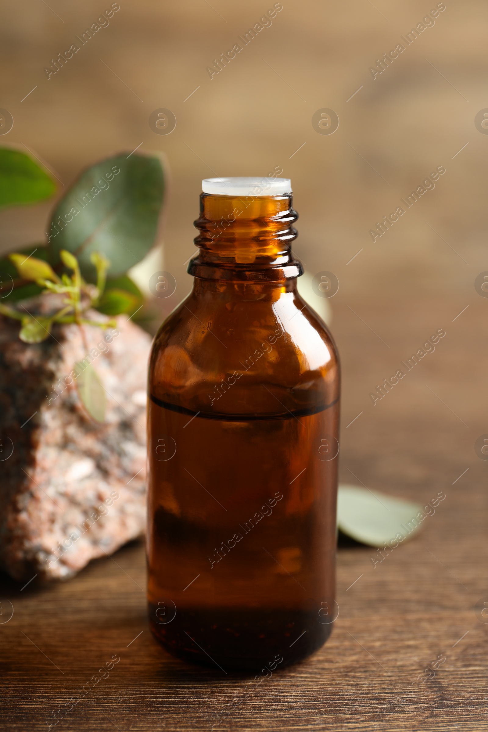 Photo of Bottle of eucalyptus essential oil, stone and leaves on wooden table