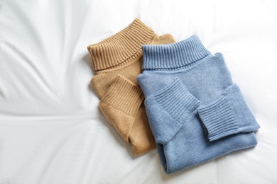 Photo of Stylish knitted sweaters on white fabric, flat lay