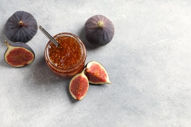 Glass jar with tasty sweet jam and fresh figs on light grey table, flat lay. Space for text