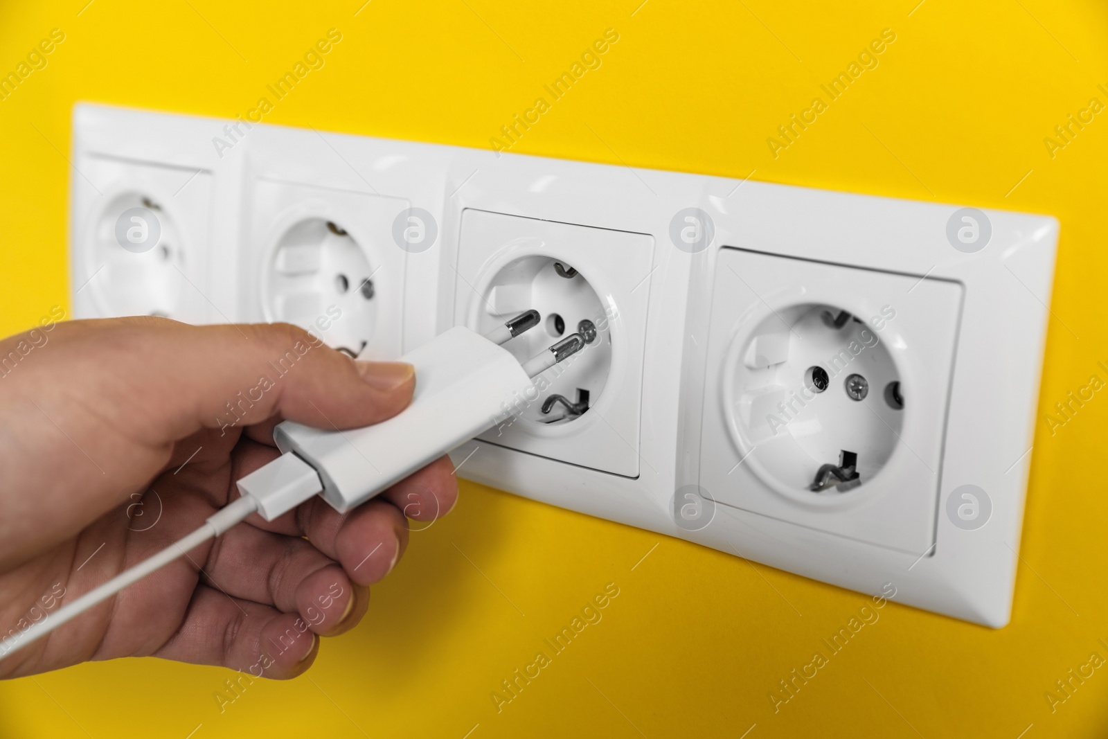 Photo of Woman plugging charger into power socket on yellow wall, closeup. Electrical supply