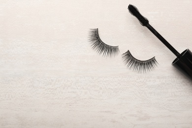 Photo of Mascara brush and artificial eyelashes on light background, top view with space for text