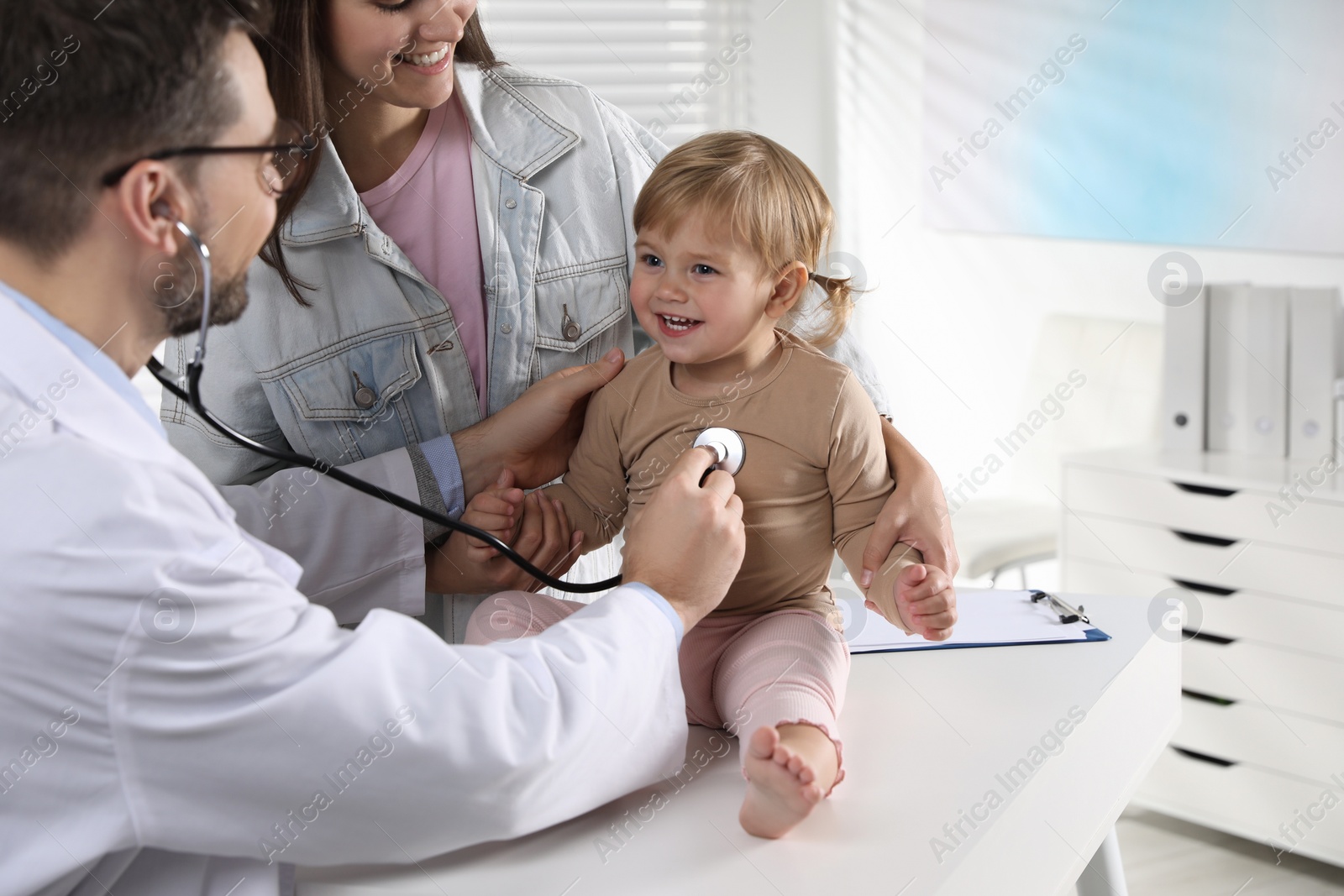 Photo of Mother and her cute baby having appointment with pediatrician in clinic. Doctor examining little girl