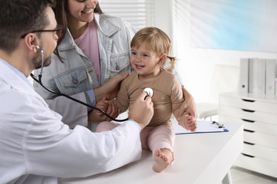 Photo of Mother and her cute baby having appointment with pediatrician in clinic. Doctor examining little girl