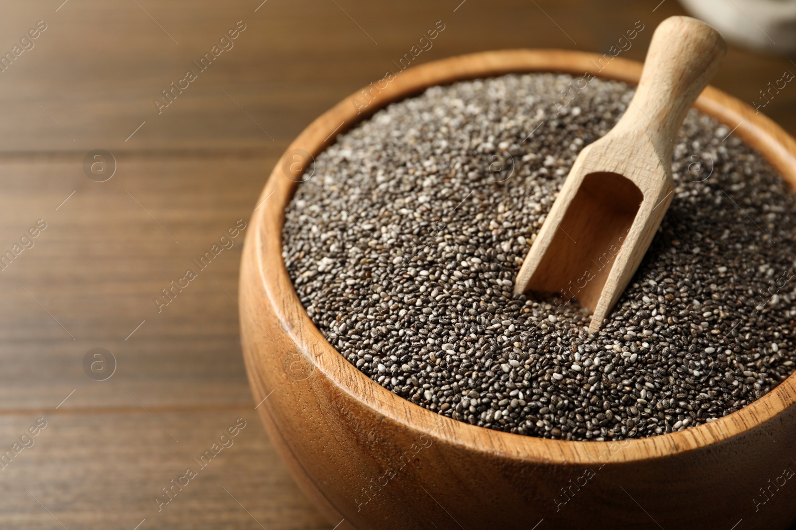 Photo of Wooden bowl with chia seeds and scoop on table, closeup
